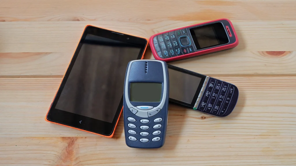 Ein Foto mit mehreren Nokia-Handys, darunter ältere Modelle mit Tasten und robuste Designs. Die Geräte sind in verschiedenen Farben und Größen angeordnet, symbolisierend klassische Mobiltelefontechnologie.