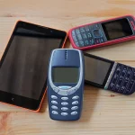 Ein Foto mit mehreren Nokia-Handys, darunter ältere Modelle mit Tasten und robuste Designs. Die Geräte sind in verschiedenen Farben und Größen angeordnet, symbolisierend klassische Mobiltelefontechnologie.